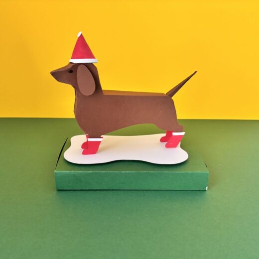 Kit créatif original permettant de créer un teckel et ses accessoires. Ici il a revêtu un bonne et des bottes de Noël