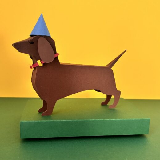 Kit de paper art pour créer un teckel et ses accessoires. Ici, il a revêtu un chapeau d'anniversaire